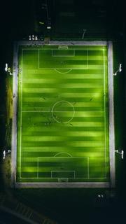 Birds eye view of a green football pitch with lights by night